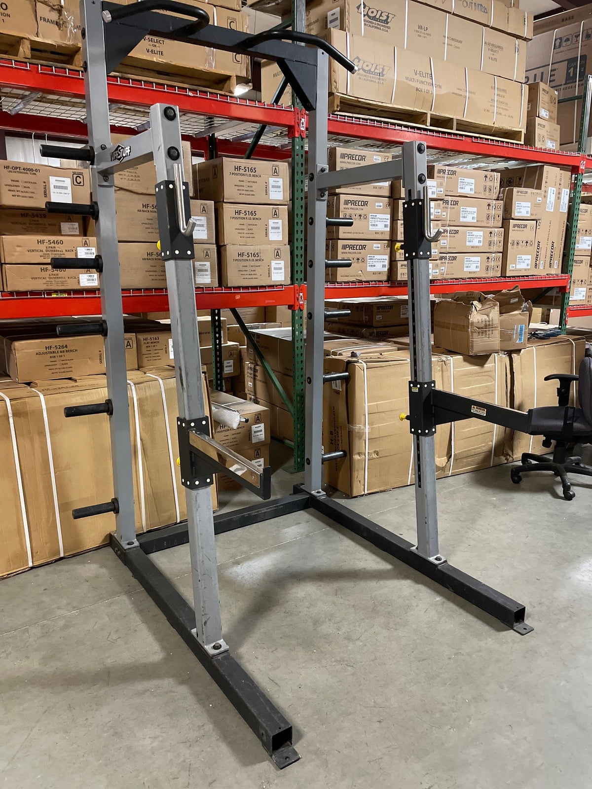 Used Tuff Stuff commercial half rack, gray uprights on black base with pull-up bar, front three-quarter view in a warehouse
